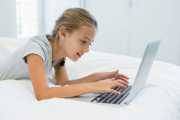 istock Smiling girl lying on bed and using laptop in bedroom 667049600