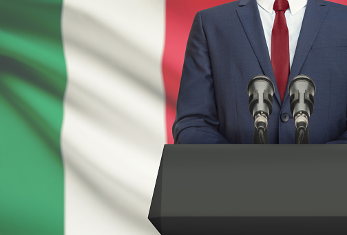 Businessman or politician making speech from behind the pulpit with national flag on background - Italy