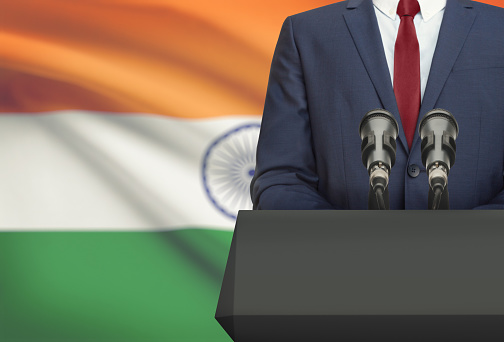 Businessman or politician making speech from behind the pulpit with national flag on background - India