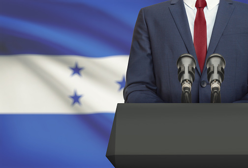 Businessman or politician making speech from behind the pulpit with national flag on background - Honduras