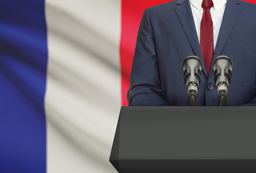 Businessman or politician making speech from behind the pulpit with national flag on background - France