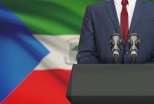Businessman or politician making speech from behind the pulpit with national flag on background - Equatorial Guinea