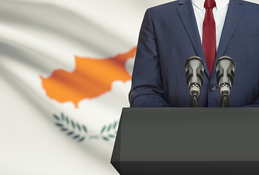 Businessman or politician making speech from behind the pulpit with national flag on background - Cyprus