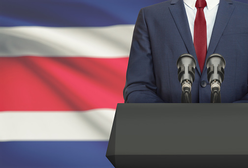 Businessman or politician making speech from behind the pulpit with national flag on background - Costa Rica