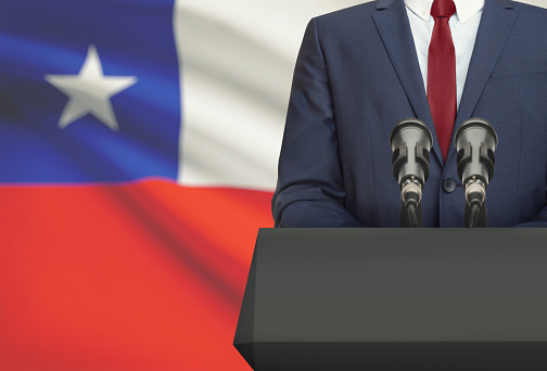 Businessman or politician making speech from behind the pulpit with national flag on background - Chile
