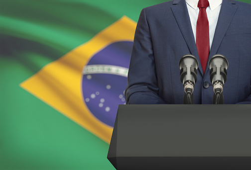 Businessman or politician making speech from behind the pulpit with national flag on background - Brazil
