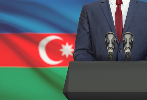 Businessman or politician making speech from behind the pulpit with national flag on background - Azerbaijan