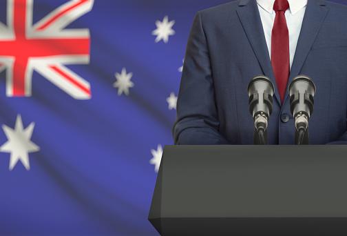 Businessman or politician making speech from behind the pulpit with national flag on background - Australia