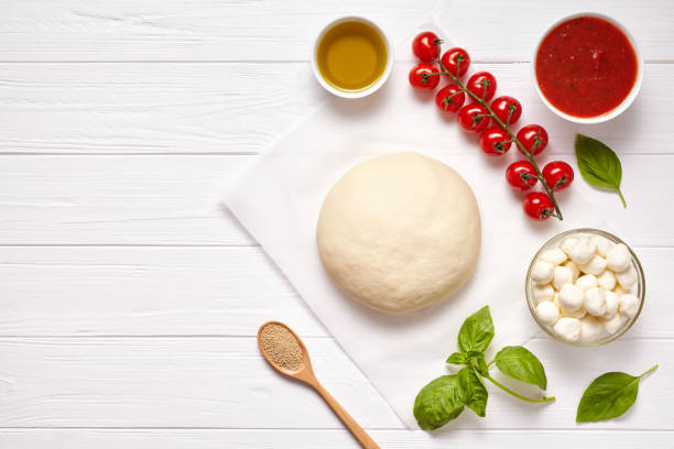 istock Raw pizza dough with baking ingredients: dough, mozzarella, tomatoes sauce, basil, olive oil, cheese, spices. Italian margherita on wooden table. Italian pizza margarita 667076770