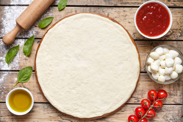 Raw dough for pizza with ingredient: tomato sauce, dough, mozzarella, tomatoes, basil, olive oil, spices served on rustic wooden table. Aerial shot, copyspace for text. stock photo