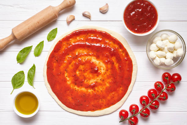 istock Pizza cooking preparation. Raw pizza dough with baking ingredients: tomatoes sauce, mozzarella, basil, olive oil, cheese, spices.Italian food cuisine background. Flat lay. 667079424