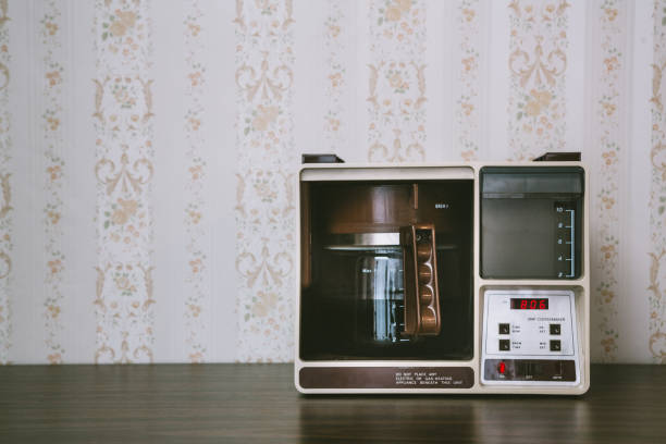 Coffee Maker in Retro Style A vintage looking automatic coffee machine sits on the counter of a 1970's / 1980's style kitchen with floral wallpaper.  Brown and yellow color theme.   Horizontal with copy space. coffee maker in kitchen stock pictures, royalty-free photos & images