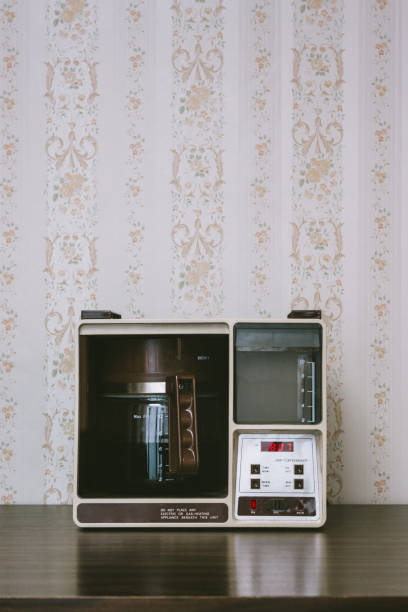Coffee Maker in Retro Style A vintage looking automatic coffee machine sits on the counter of a 1970's / 1980's style kitchen with floral wallpaper. Brown and yellow color theme. Horizontal with copy space. early 20th century kitchen stock pictures, royalty-free photos & images