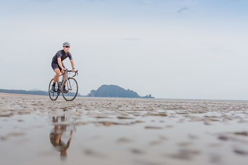 Young asian cyclist man ride  bicycle  the beach at the sunset
