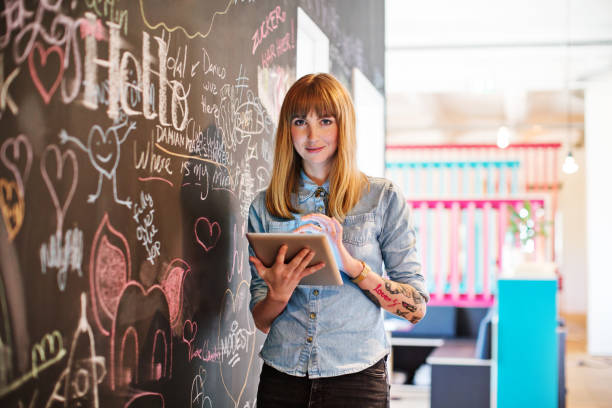 Businesswoman using digital tablet by blackboard Portrait of beautiful businesswoman using digital tablet in office. Female professional is standing by scribbled blackboard. She is wearing smart casuals at workplace. hipsters stock pictures, royalty-free photos & images