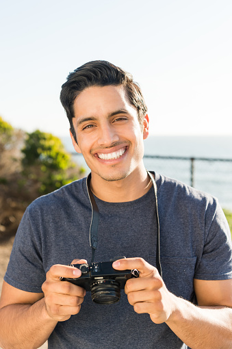 Handsome hispanic man taking a photo at the ocean on a summer day.