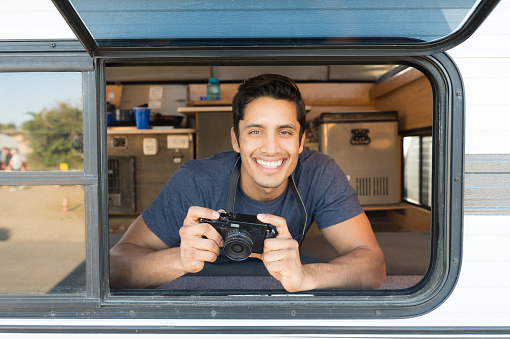Handsome hispanic man taking a photo out the window of his camper on a summer day.