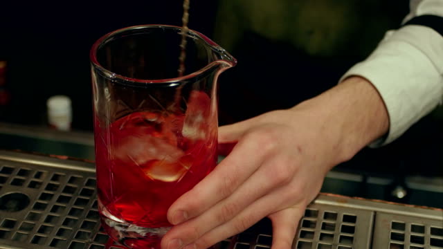 Barman mixing red spritz aperitif aperol cocktail with ice cubes and pouring it into an empty glass