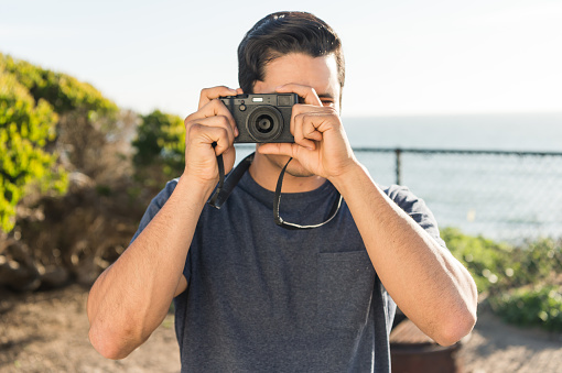 Handsome hispanic man taking a photo at the ocean on a summer day.