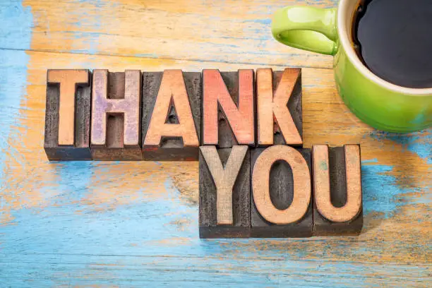 thank you phrase in vintage letterpress wood type printing blocks stained by color inks with a cup of coffee