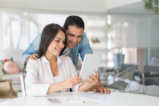 Happy Latin American couple at home looking at a tablet computer watching a video - lifestyle concepts