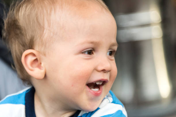 Funny baby with evil genius laugh portrait photo. Adorable infant with shiny blond hair, big light eyes, plump cheeks and wide open mouth looks up.