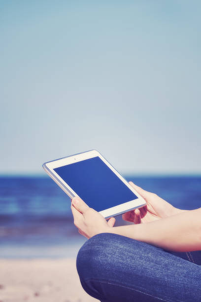 istock Color toned close up of female hands with tablet computer on a beach. 667148690