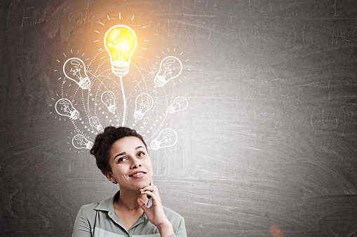 Portrait of a beautiful African American woman is standing near a blackboard with a bunch of light bulbs. One shines. Mock up.