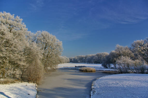Frozen river in a park with snow-covered fields and trees