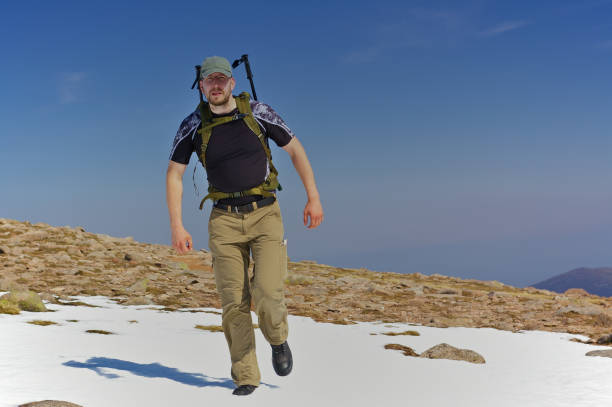 Hiker with backpack crossing a snowfield in the mountains stock photo