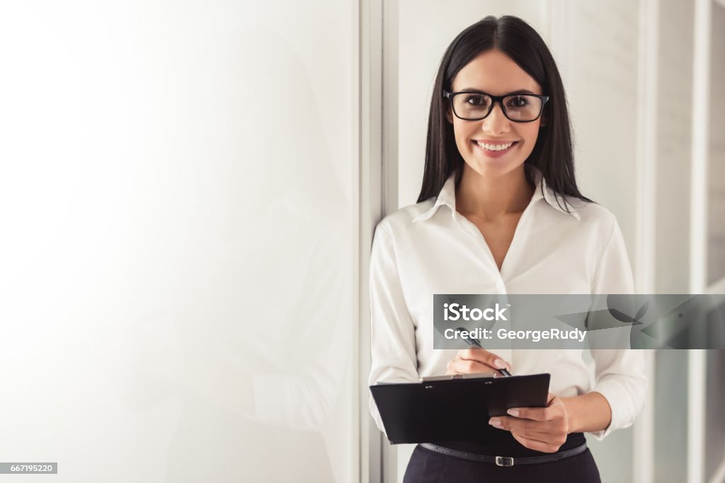 Beautiful young psychotherapist Beautiful young psychotherapist is making notes, looking at camera and smiling while standing in office Mental Health Professional Stock Photo