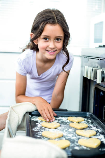 istock Girl smiling while touching heart shape cookies in tray 667218752