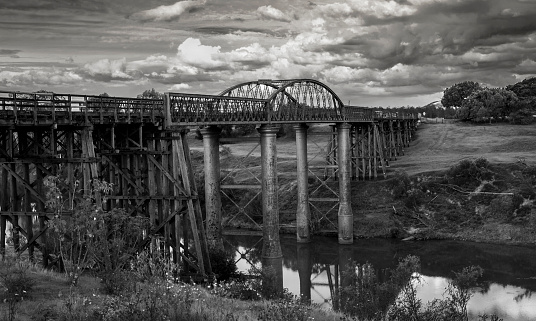 Nineteenth century rail and truss bridge crossing river with storm clouds overhead.
