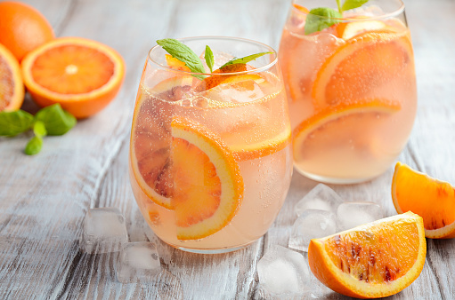 Cold refreshing drink with blood orange slices in a glass on a wooden background. Selective focus, copy space.