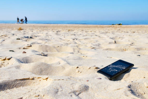 teléfono móvil con pantalla rota en la arena en una playa. - lost beach fotografías e imágenes de stock