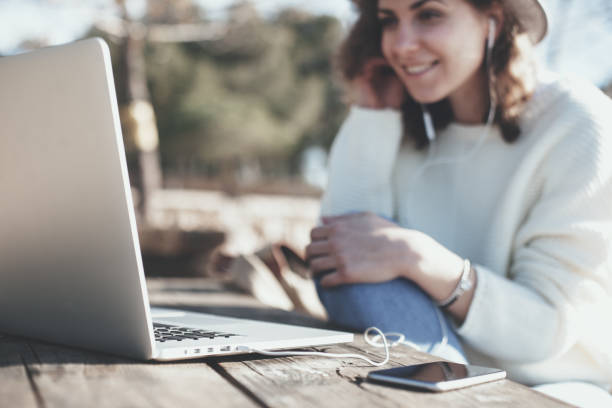 Female traveler sitting at picnic table with mobile phone and laptop stock photo