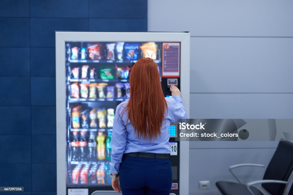 buying something in the airport rear view of business woman inside airport sitting in front of vending machine and buying some snack.lifestyle shot. Vending Machine Stock Photo