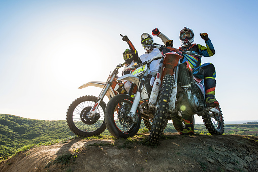 Low angle view of three motocross riders on stunt bikes on top of hill with hands raised.