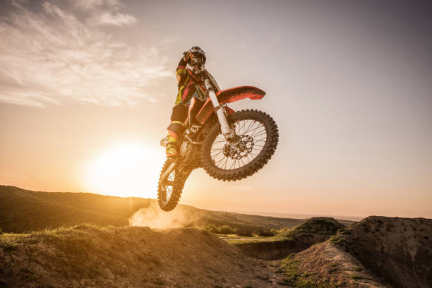 Low angle view of man on dirt bike jumping at sunset on off-road terrain.