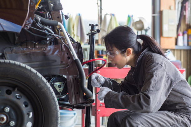 mujer mecánico arreglando un coche dañado en un taller de reparación de automóviles - car auto repair shop repairing accident fotografías e imágenes de stock