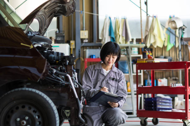 Female mechanic inspecting a damaged car in an auto repair garage stock photo
