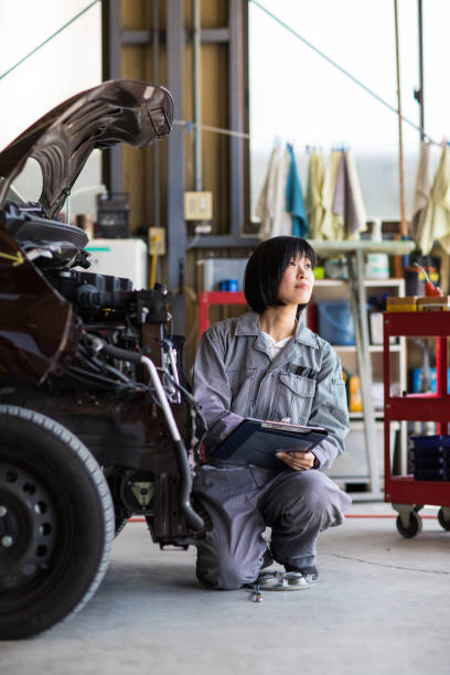 Female mechanic inspecting a damaged car in an auto repair garage stock photo