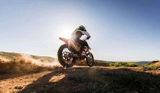 Motocross rider driving fast while racing on dirt track. Rear view of man on dirt bike riding fast on off-road dirt track. motorcycle racing stock pictures, royalty-free photos & images
