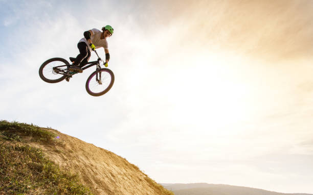 Below view of extreme cyclist jumping against the sky. Low angle view of skillful mountain bike rider jumping at sunset against the sky. Copy space. x games stock pictures, royalty-free photos & images