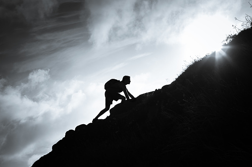 Black and white image of man climbing up a mountain.