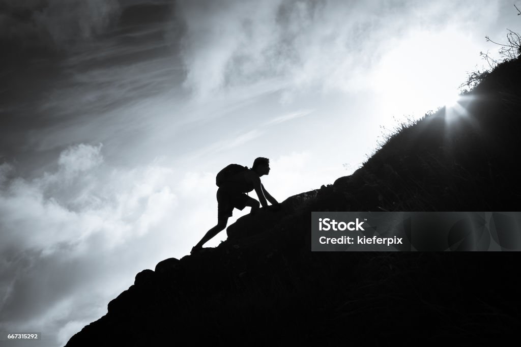 Man climbing up a mountain. Black and white image of man climbing up a mountain. Mountain Stock Photo