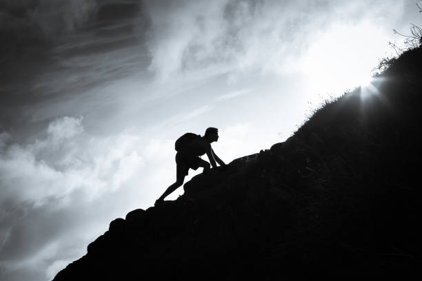 Man climbing up a mountain. Black and white image of man climbing up a mountain. steep stock pictures, royalty-free photos & images