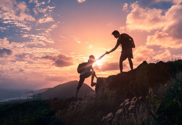 Helping hikers Male and female hikers climbing up mountain cliff and one of them giving helping hand. male meaning stock pictures, royalty-free photos & images
