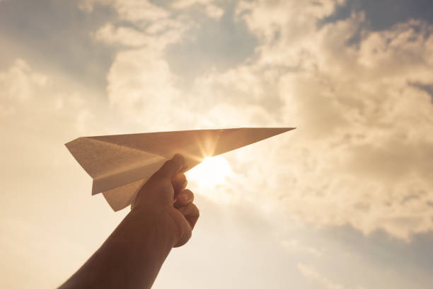 Taking flight! Hand holding paper airplane in the sky. taking off activity photos stock pictures, royalty-free photos & images