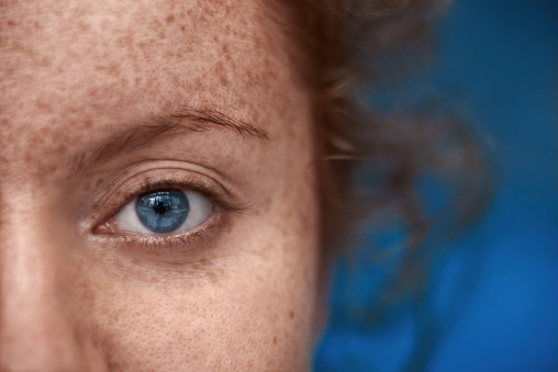 close up shot of woman with blue eye looking at camera, freckels on her skin, red hair.